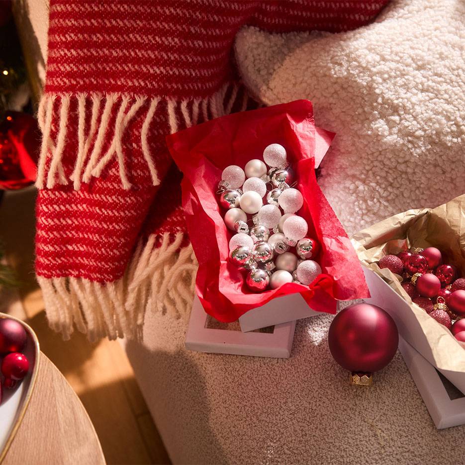 Decorazioni natalizie: palline rosse e argentate in scatole, con coperta e cuscino.