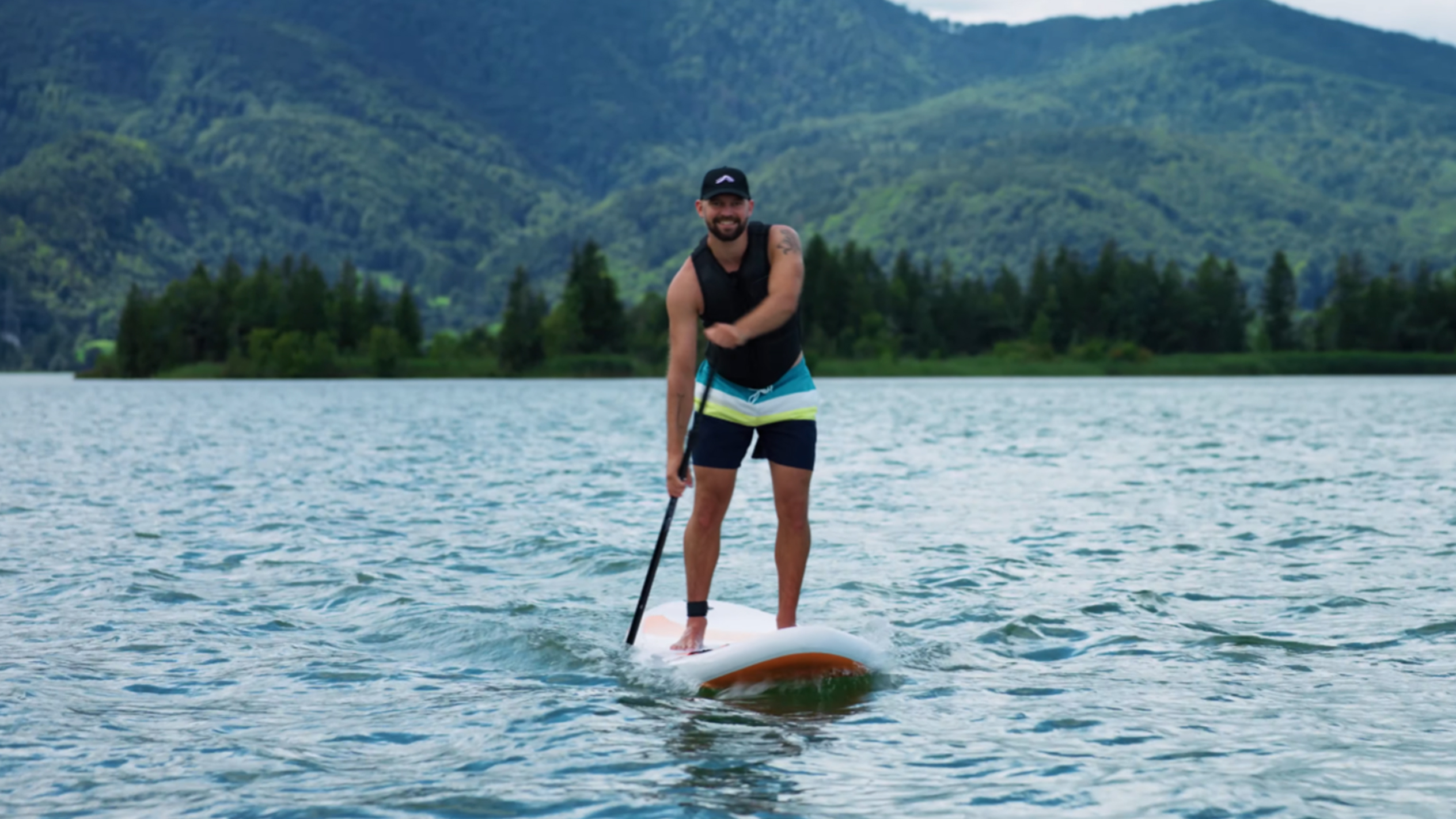 Uomo su tavola da paddle surf in un lago con montagne sullo sfondo.