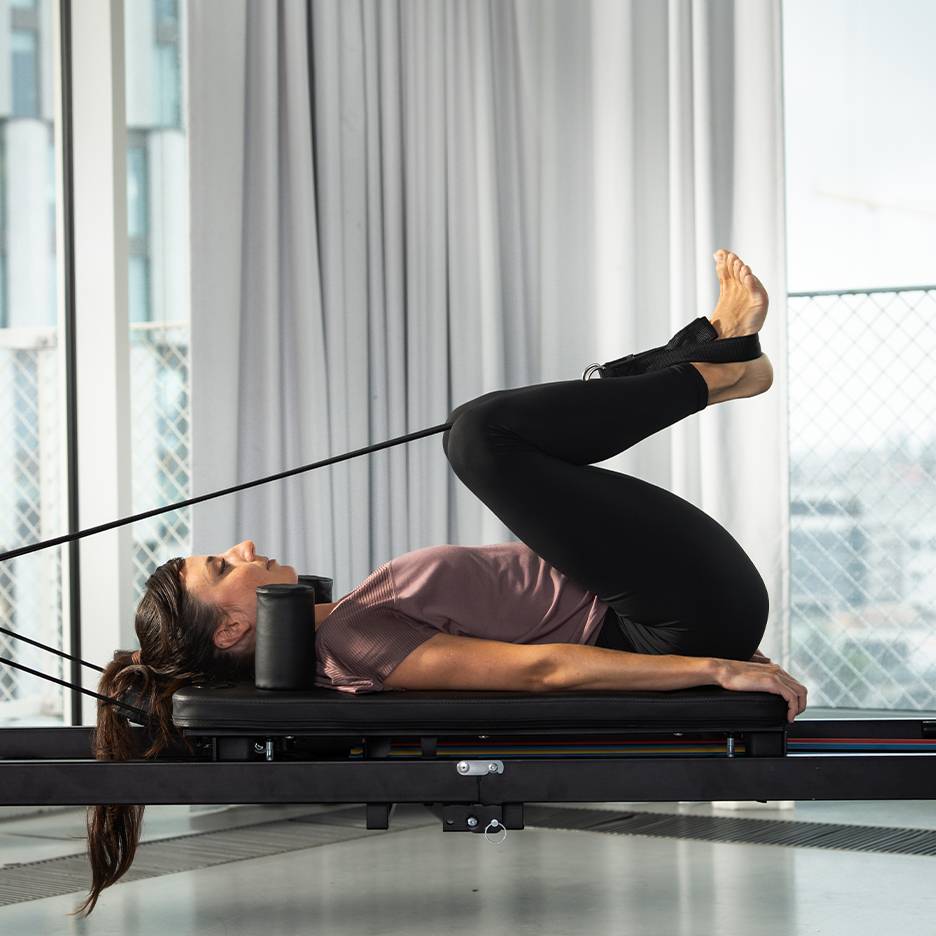 Donna che fa Pilates su un reformer con le gambe sollevate.