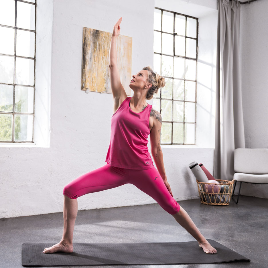 Donna che fa yoga indossando abbigliamento sportivo rosa in una stanza luminosa.