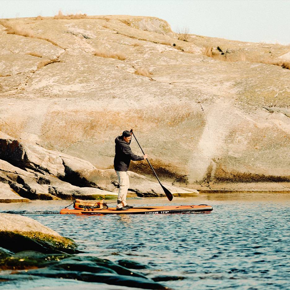 Uomo che pagaia su una tavola da stand-up paddle arancione su un lago roccioso.