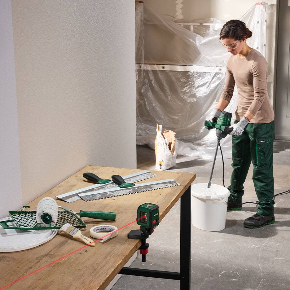 Donna che mescola materiale da costruzione con attrezzi per pittura e livellamento su un tavolo.