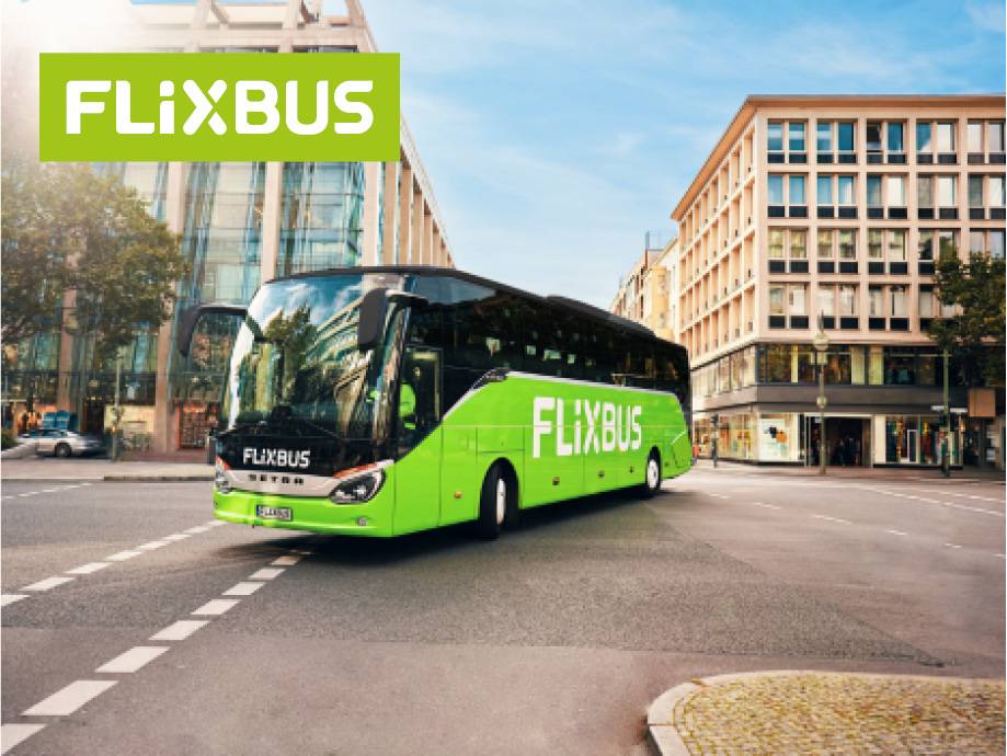 Autobus verde con logo su strada cittadina, edifici moderni sullo sfondo.
