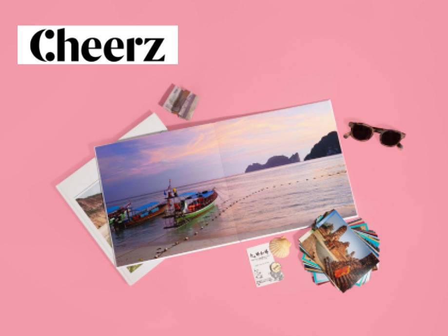 Album fotografico aperto con paesaggio marino, occhiali da sole e stampe fotografiche su sfondo rosa.