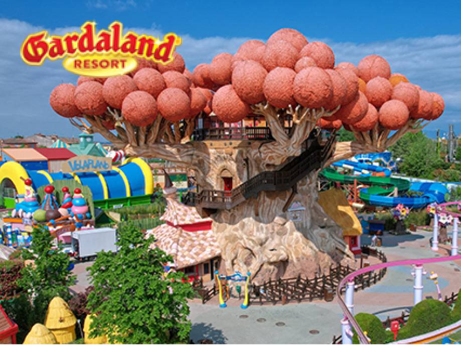 Parco divertimenti con un grande albero a tema e attrazioni colorate.