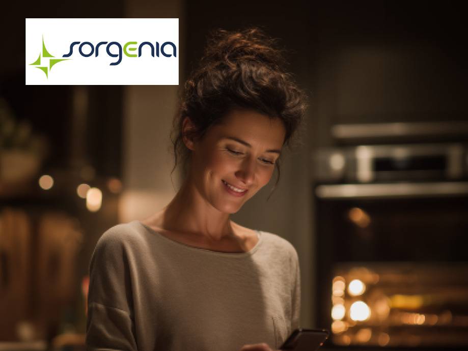 Donna sorridente che usa lo smartphone in cucina, con il logo Sorgenia in alto a sinistra.