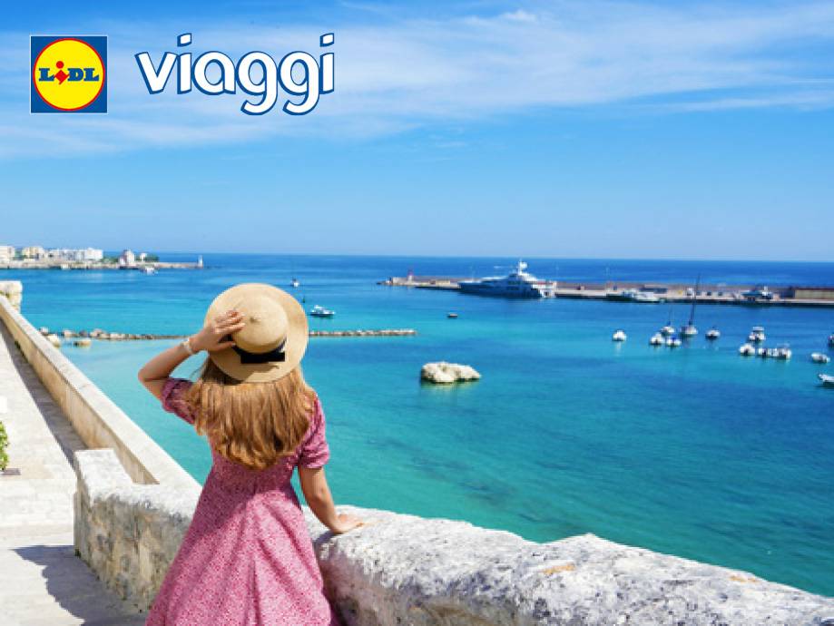 Donna con cappello di paglia guarda il mare blu con barche e città in lontananza, con testo 'viaggi'.