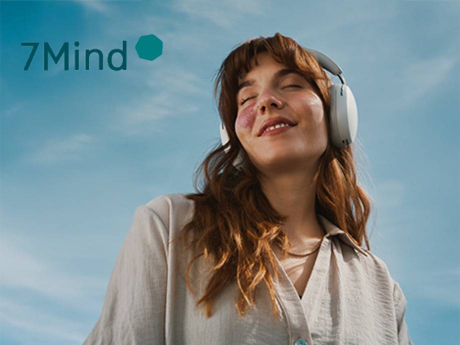 Donna sorridente con cuffie, occhi chiusi, su sfondo cielo azzurro. Testo: 7Mind.