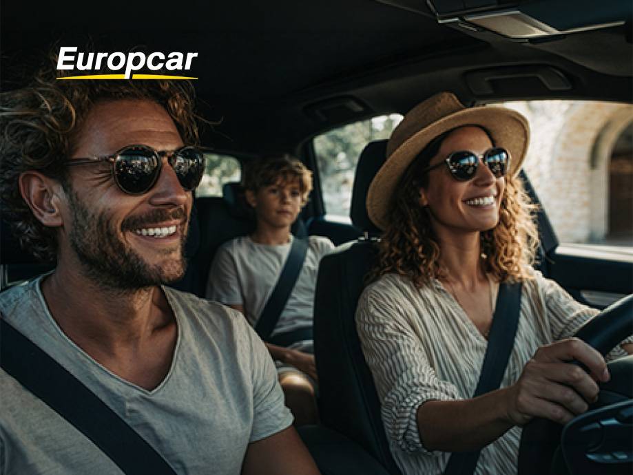 Una famiglia felice in auto, con la madre che guida e il padre e il figlio seduti dietro.