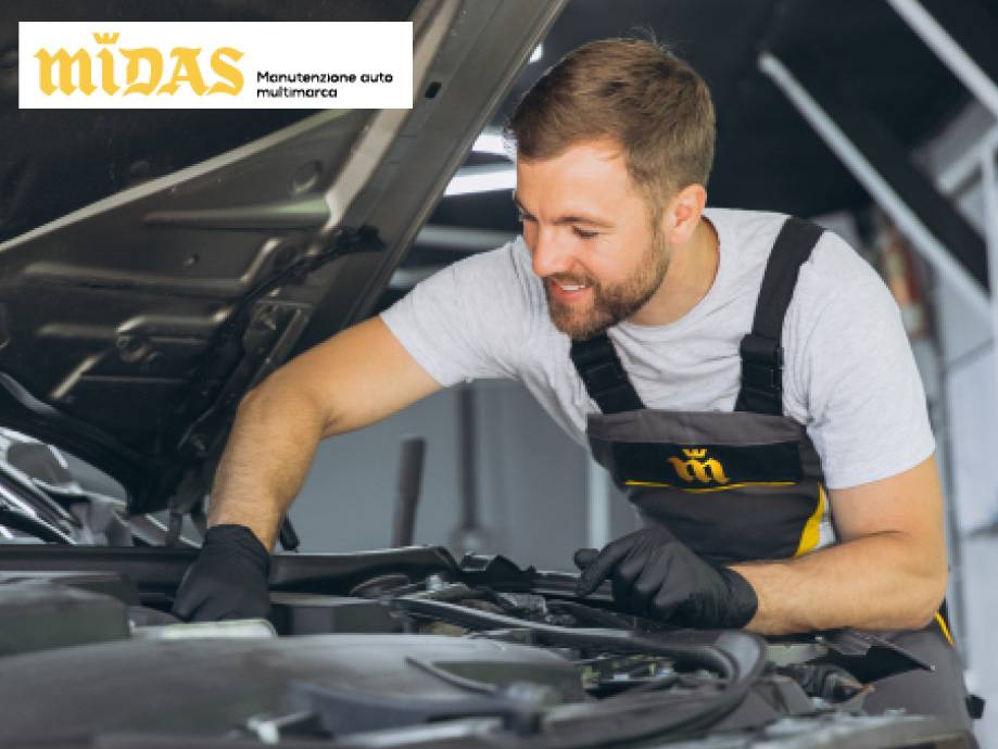 Meccanico sorridente che lavora sul motore di un'auto, con il cofano aperto.