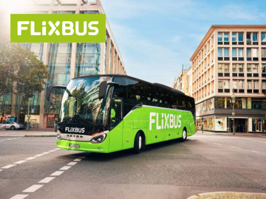 Un autobus FlixBus verde brillante su una strada cittadina con edifici sullo sfondo.