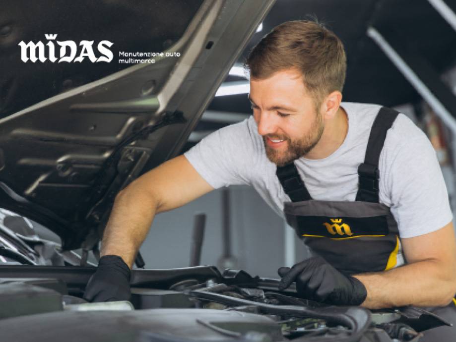 Un meccanico Midas sorridente ispeziona il motore di un'auto.