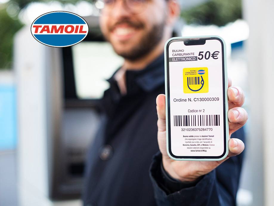 Un uomo sorridente mostra un buono carburante elettronico Tamoil da 50€ sul suo smartphone.