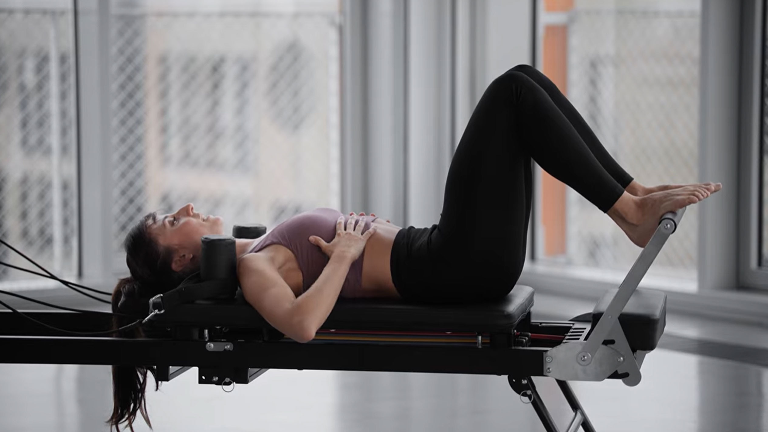 Donna che fa Pilates su un reformer, con le mani sul petto.