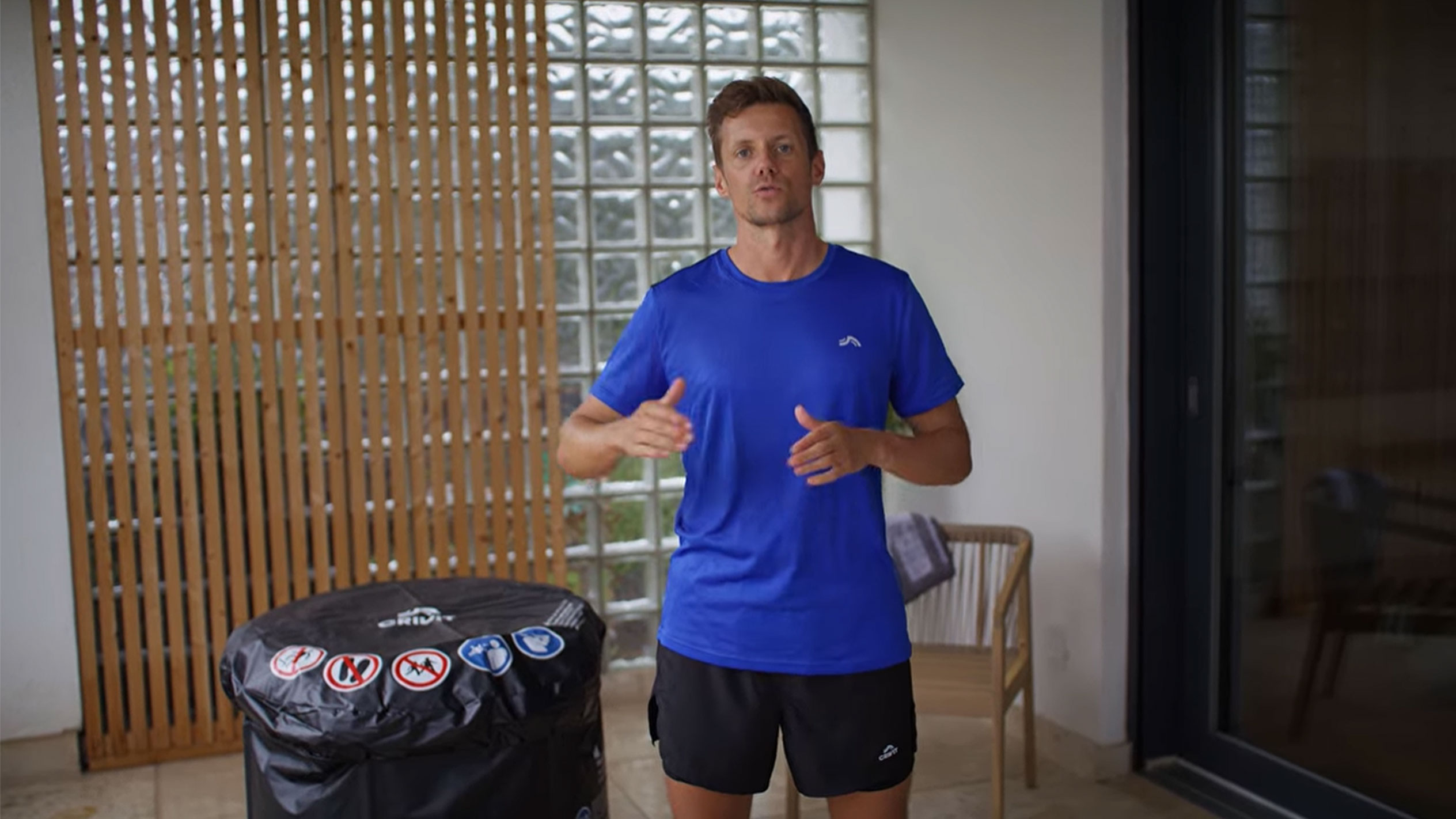 Uomo in maglietta blu e pantaloncini neri, accanto a una copertura nera per vasca idromassaggio.