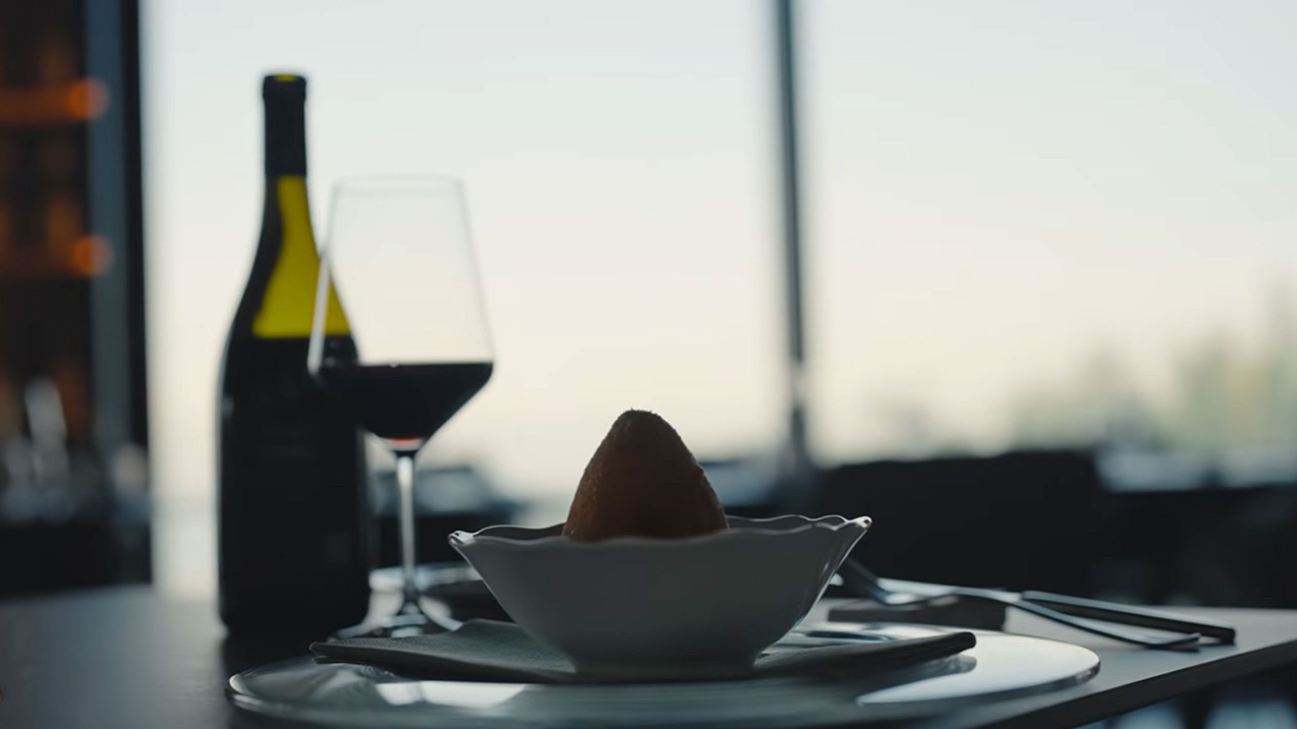 Una bottiglia di vino rosso e un bicchiere accanto a un arancino in una ciotola su un tavolo.