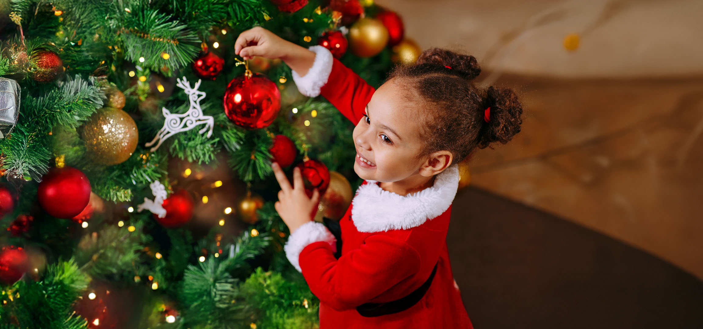 Bambina felice in costume da Babbo Natale che decora un albero di Natale con palline rosse.