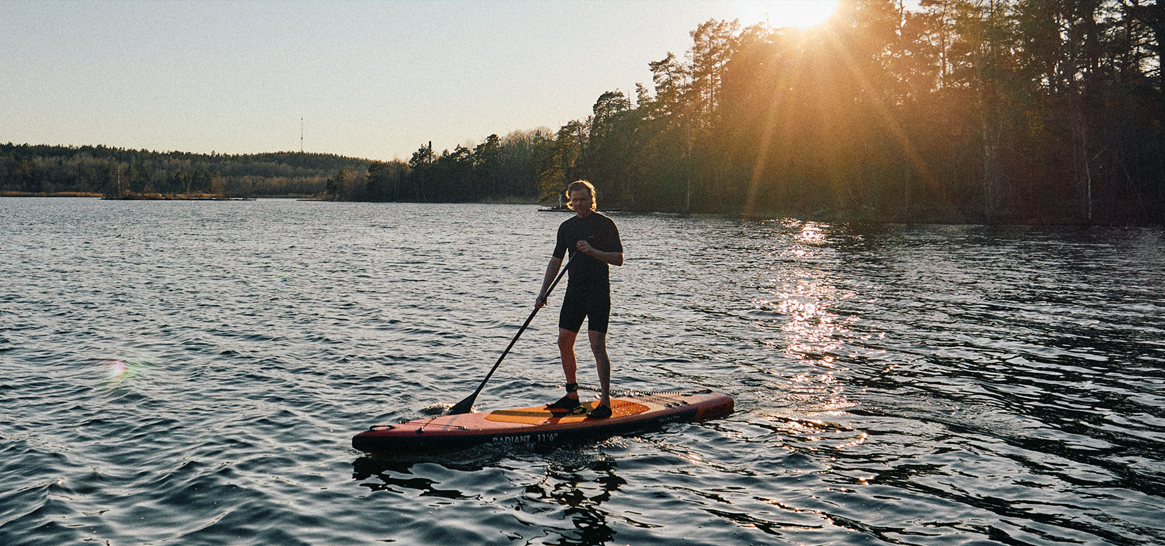 Uomo su una tavola da stand up paddle su un lago al tramonto.