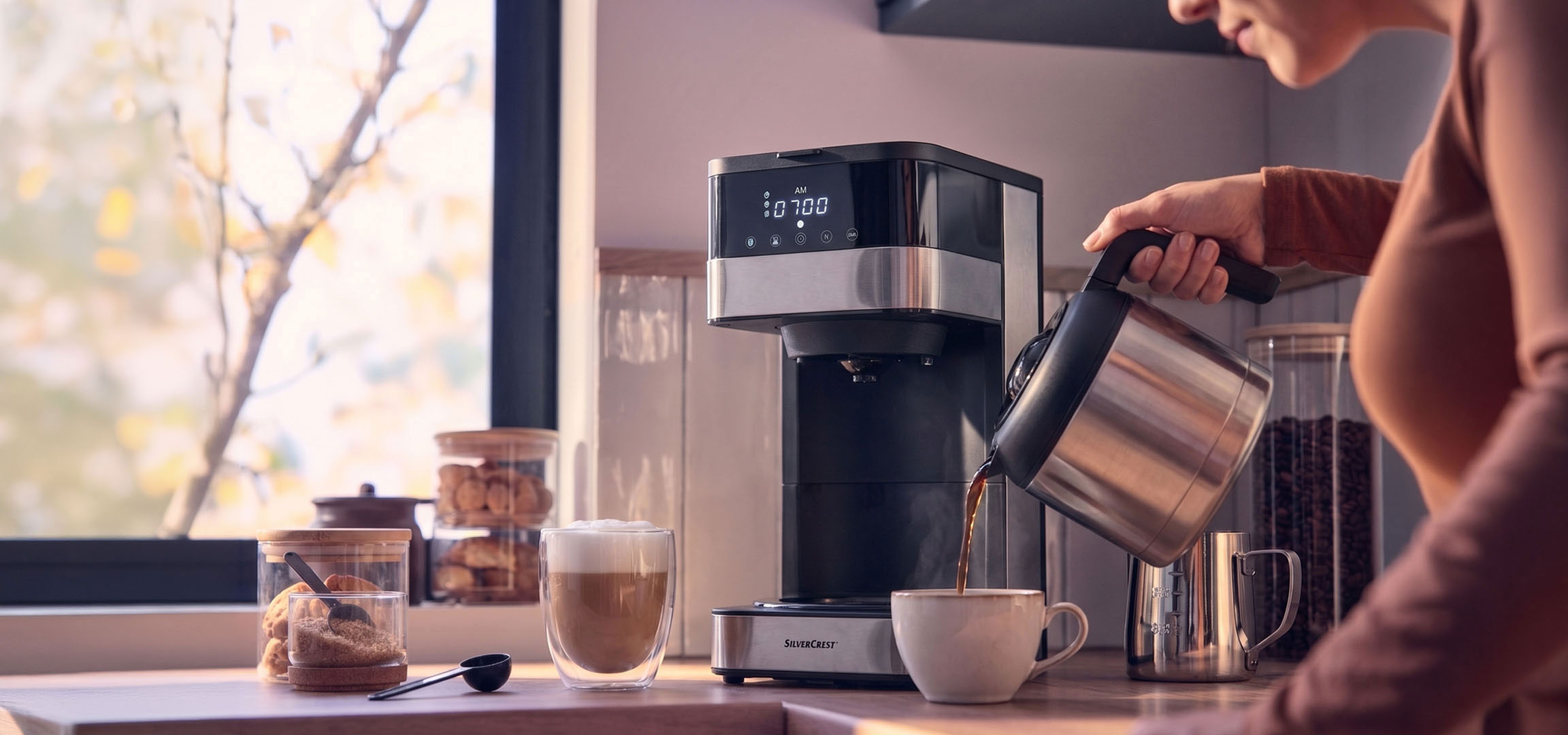 aiLabeling.aiLabelForImageAltText: Macchina da caffè che eroga caffè in una tazza, con una finestra luminosa sullo sfondo.