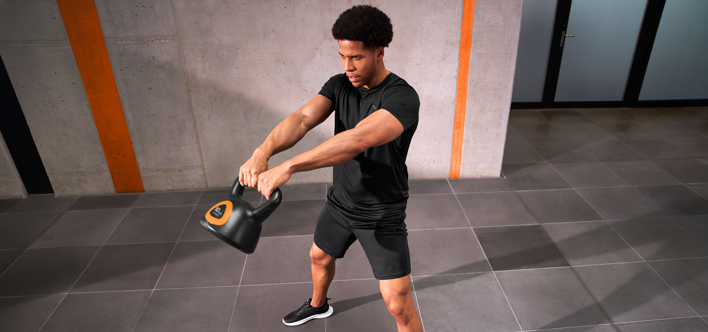 aiLabeling.aiLabelForImageAltText: Uomo che si allena con un kettlebell nero e arancione.