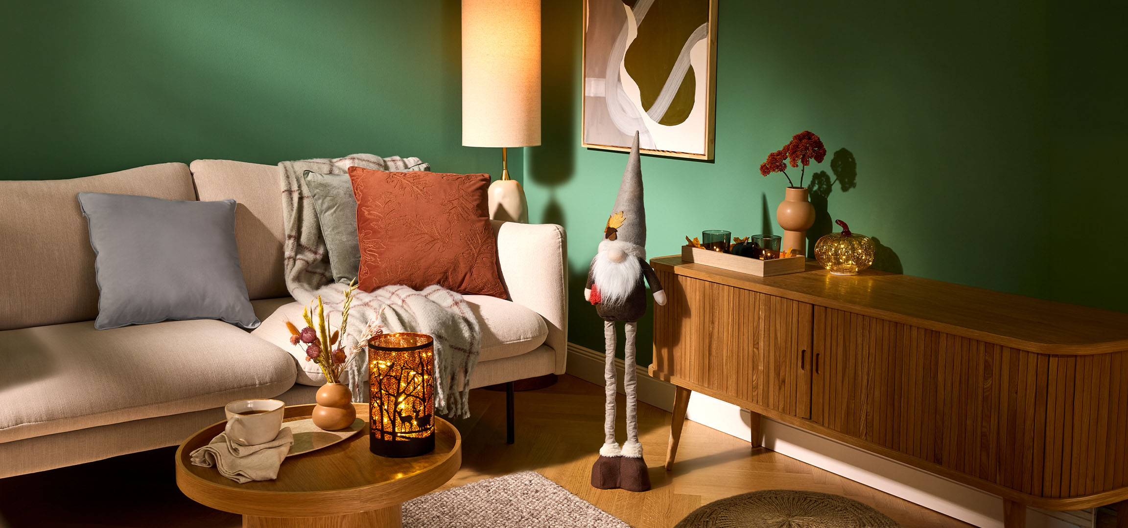 Accogliente soggiorno con divano beige, cuscini, coperta e decorazioni autunnali.