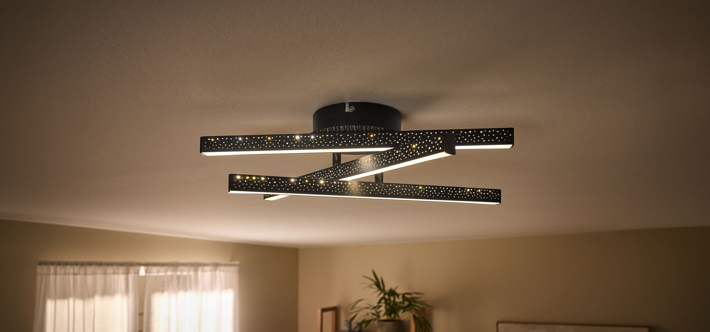 Plafoniera LED moderna con barre nere perforate e luce calda.