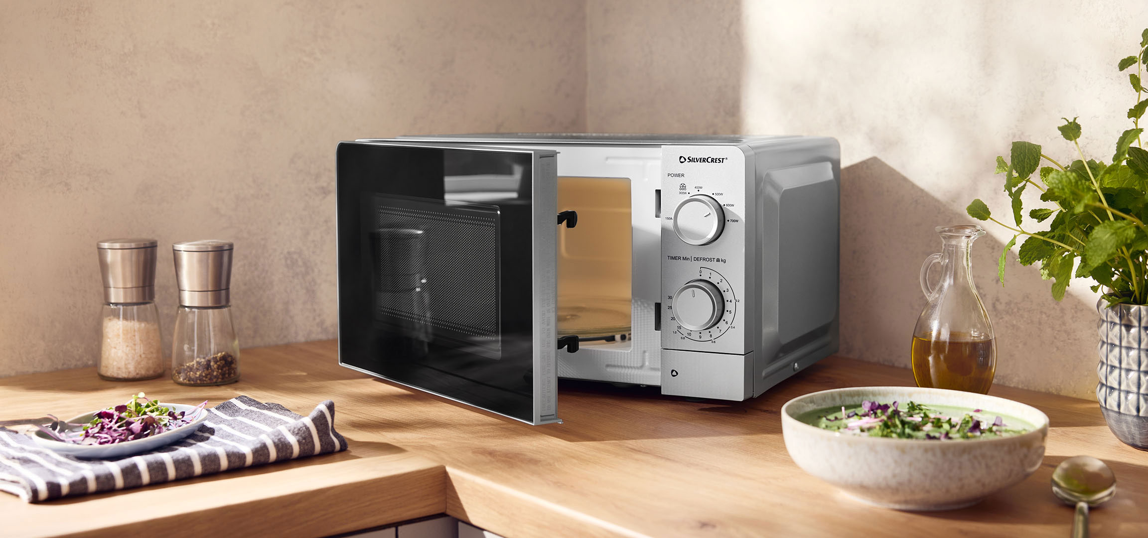 aiLabeling.aiLabelForImageAltText: Forno a microonde con porta aperta su un bancone in legno, con spezie e ciotole.