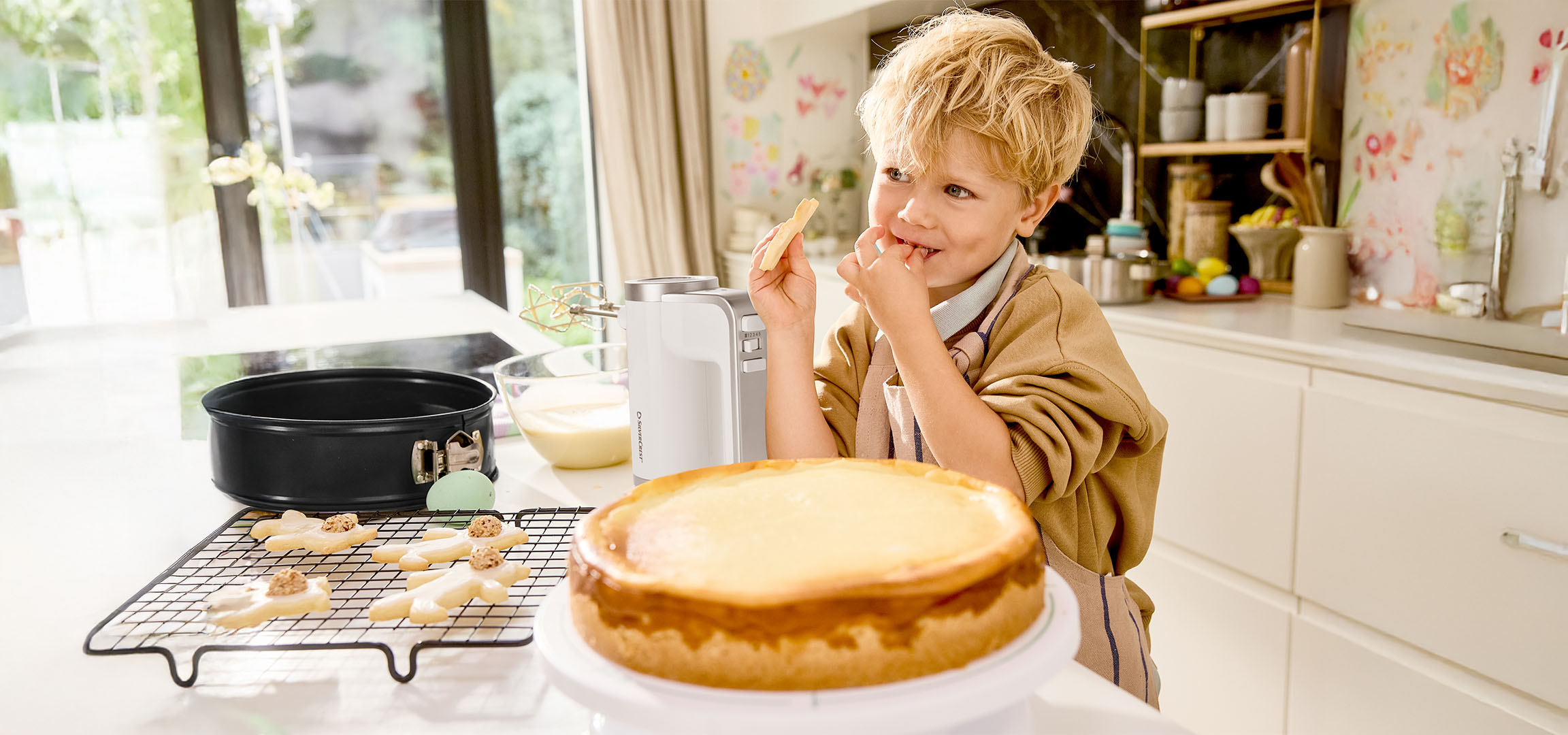 Bambino assaggia l'impasto mentre prepara una torta e biscotti in cucina.