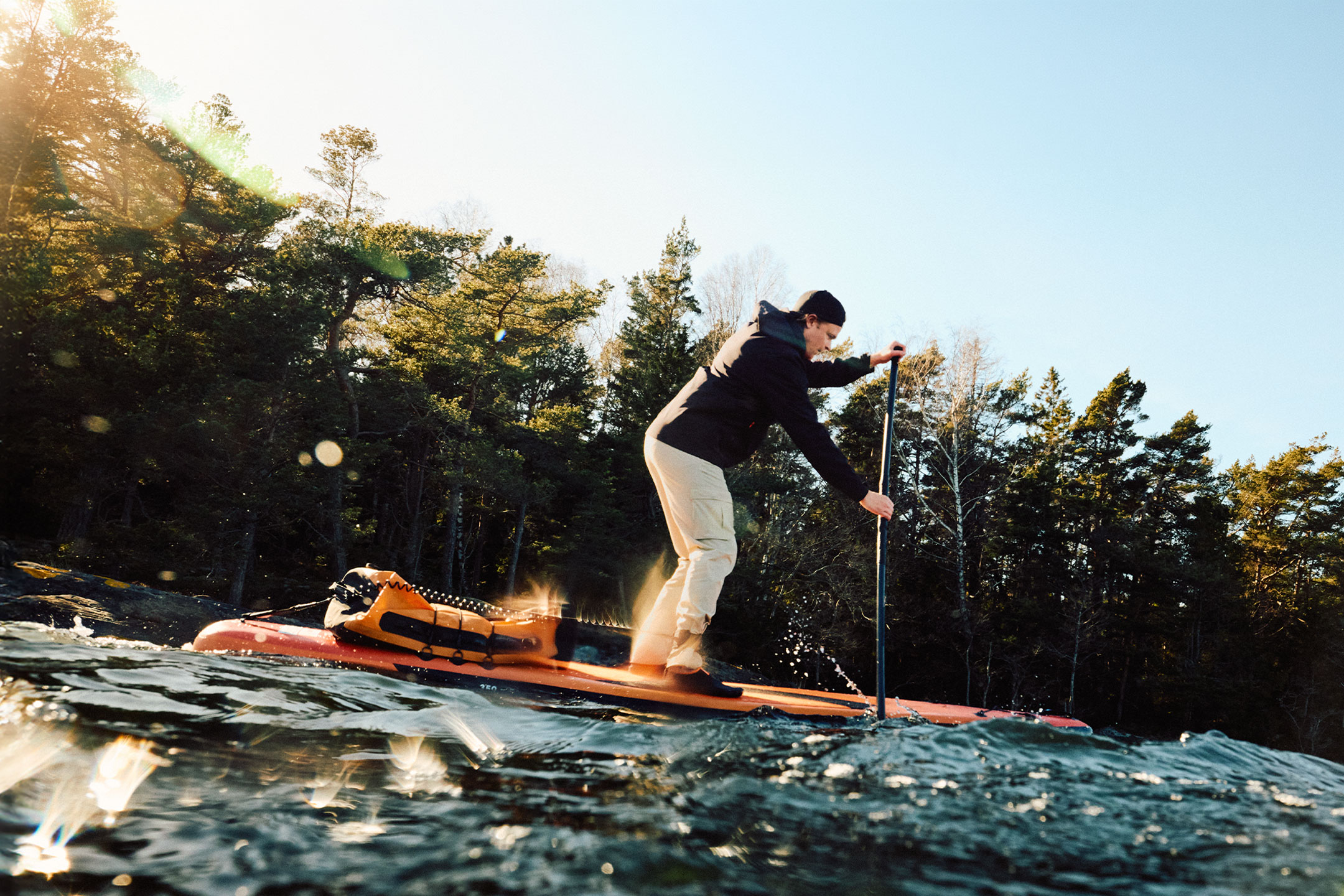 Uomo in paddleboard con una borsa stagna arancione vicino a una foresta.