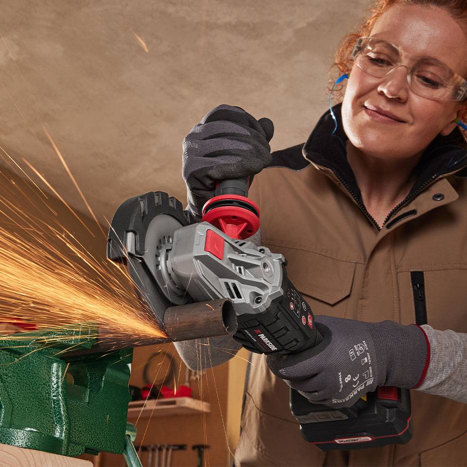Donna con occhiali di sicurezza usa una smerigliatrice angolare a batteria per tagliare un tubo metallico.