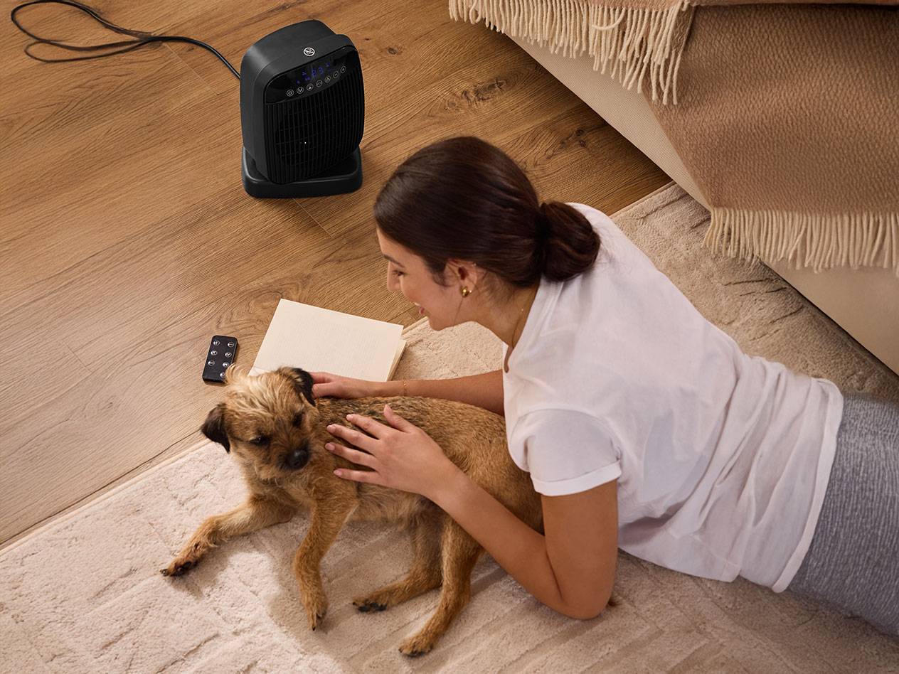 Donna che accarezza un cane accanto a un riscaldatore nero sul pavimento.