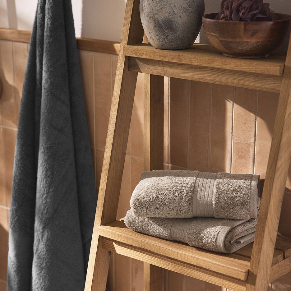 Asciugamani grigi su una mensola e una scala di legno in un bagno piastrellato.