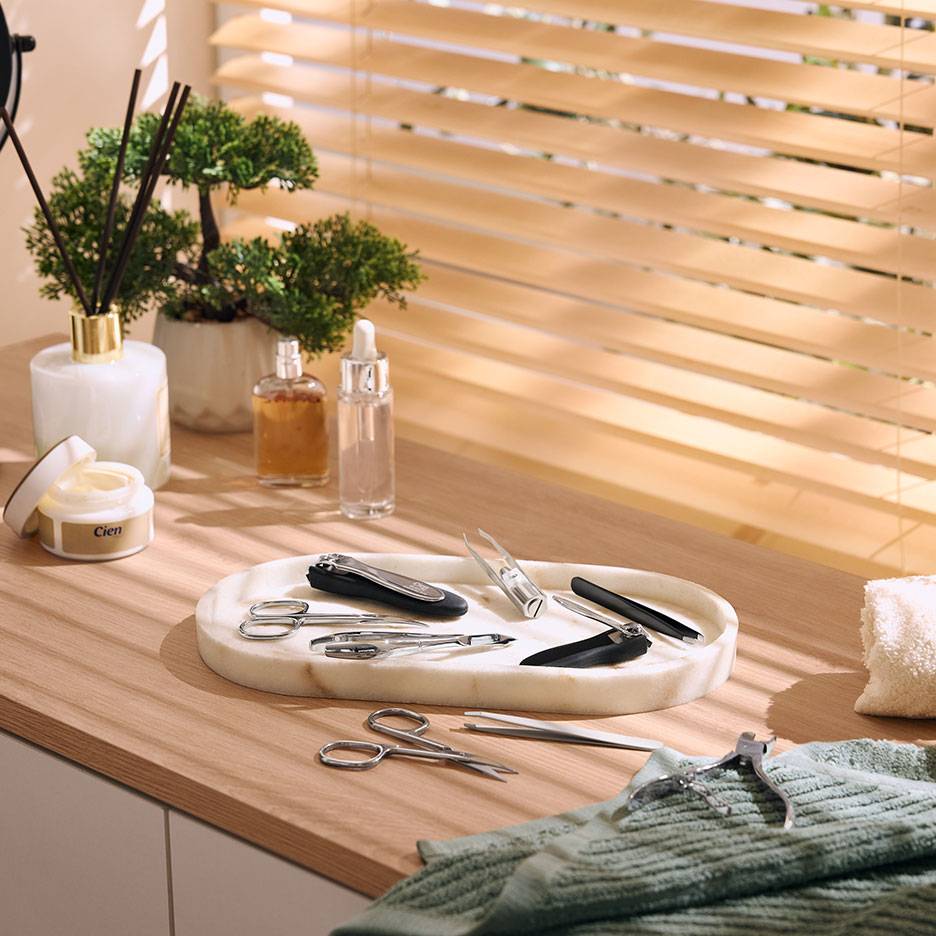 Set manicure su vassoio di marmo, con cosmetici e piante su superficie in legno.