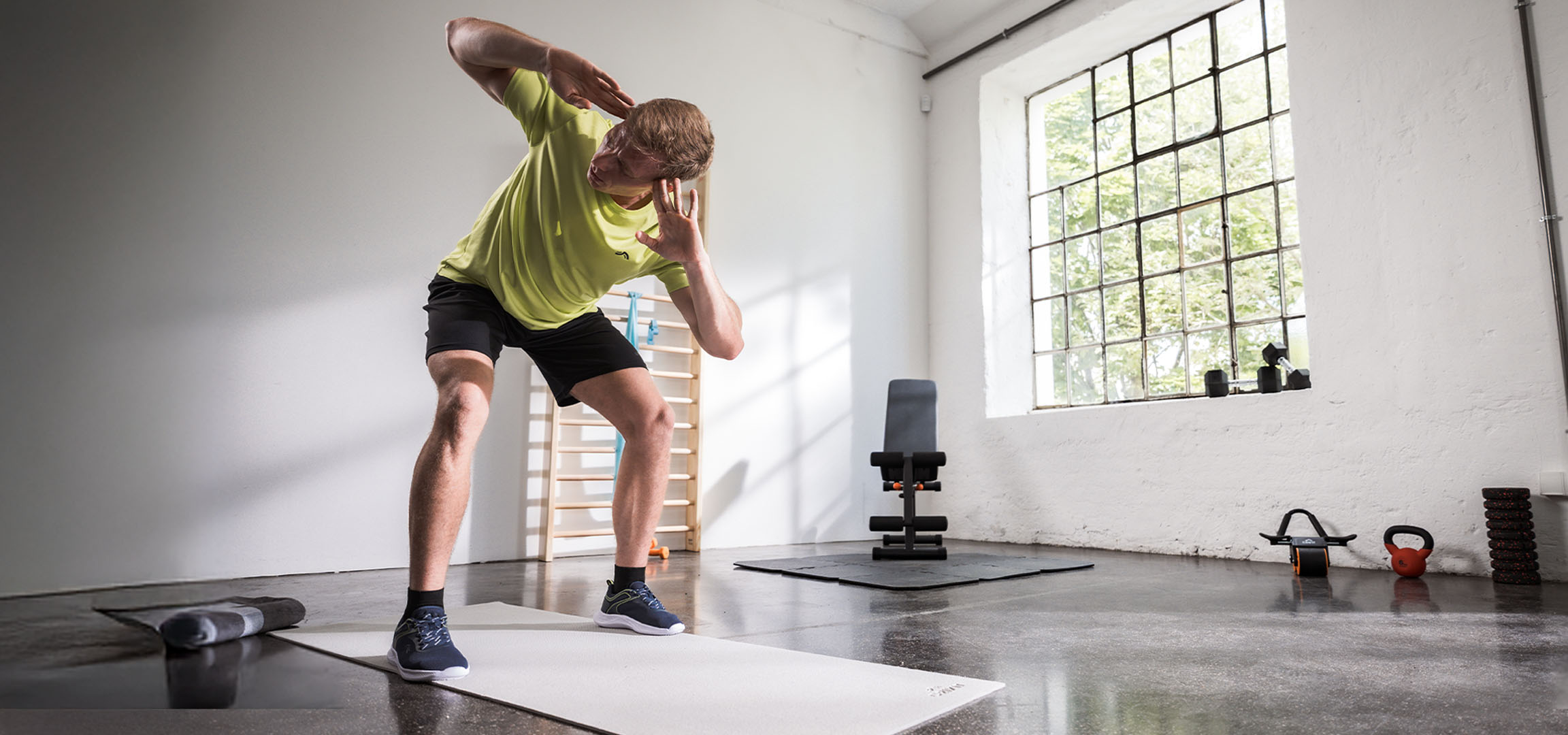 Uomo che si allena in palestra, usando un tappetino da yoga e manubri.