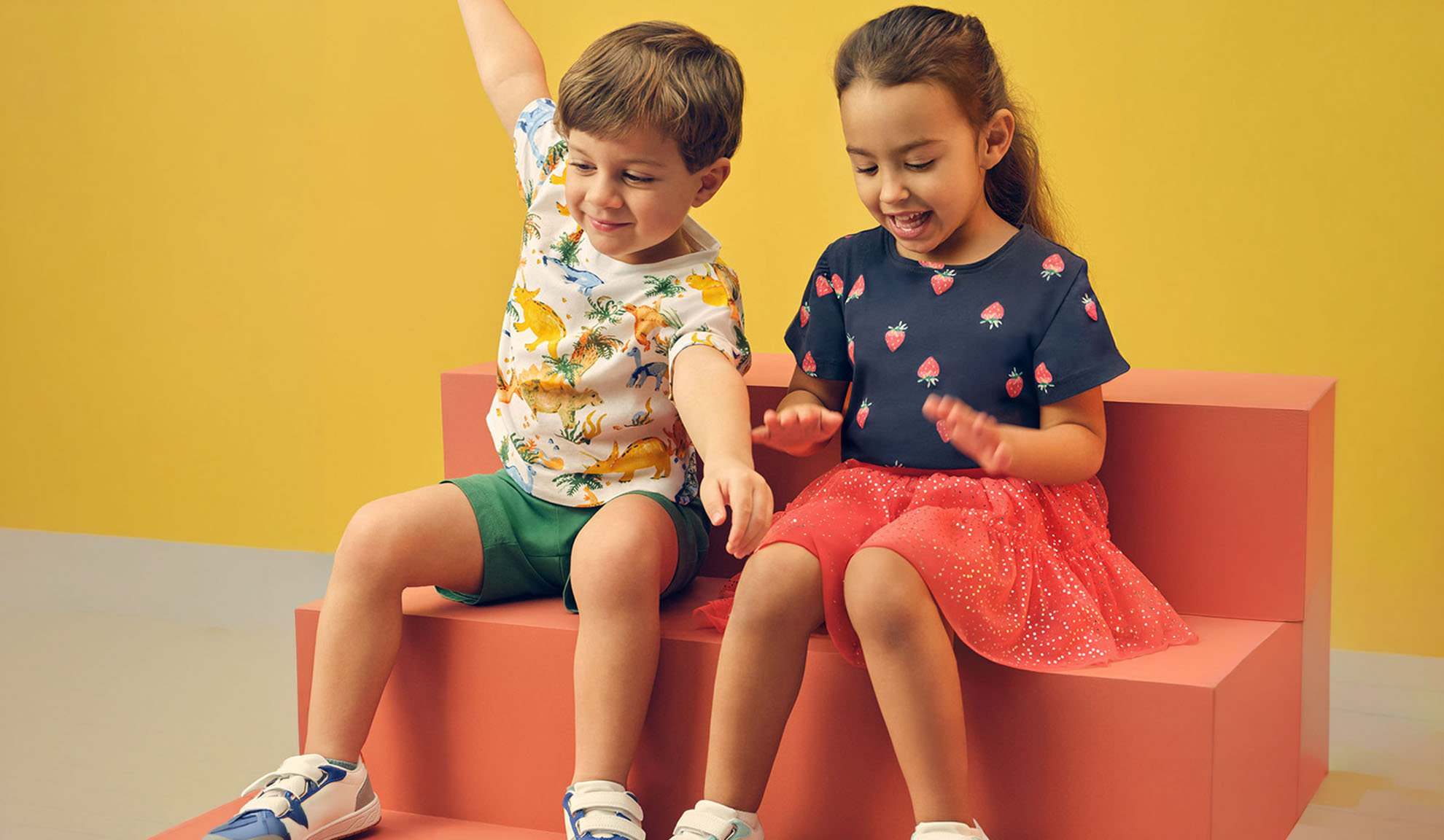 Due bambini in abiti estivi, un bambino con una maglietta di dinosauri e una bambina con una maglietta di fragole.
