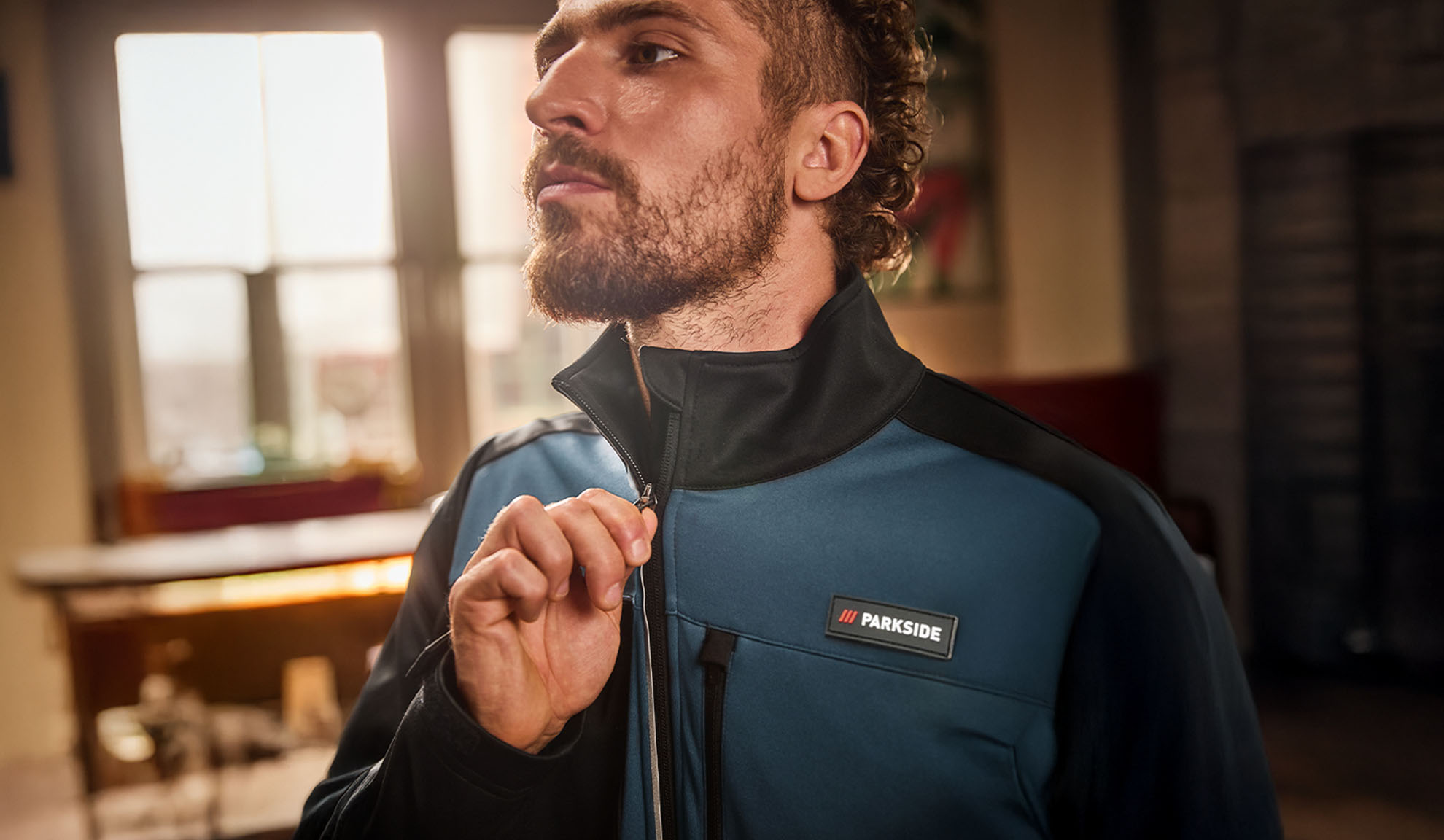Uomo con giacca da lavoro Parkside blu e nera, che la sta chiudendo.