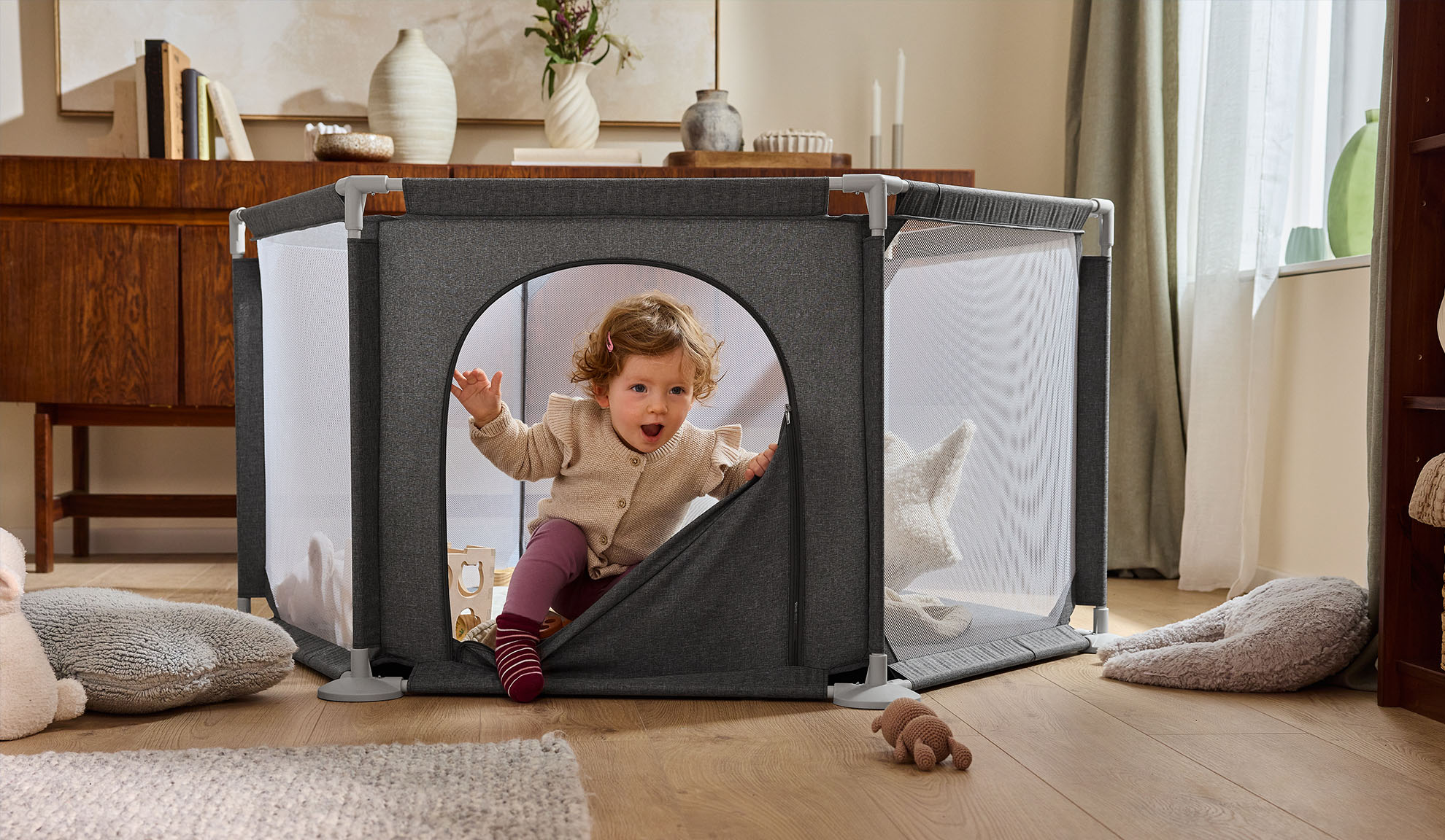 Bambino felice che esce da un box grigio in un accogliente soggiorno.