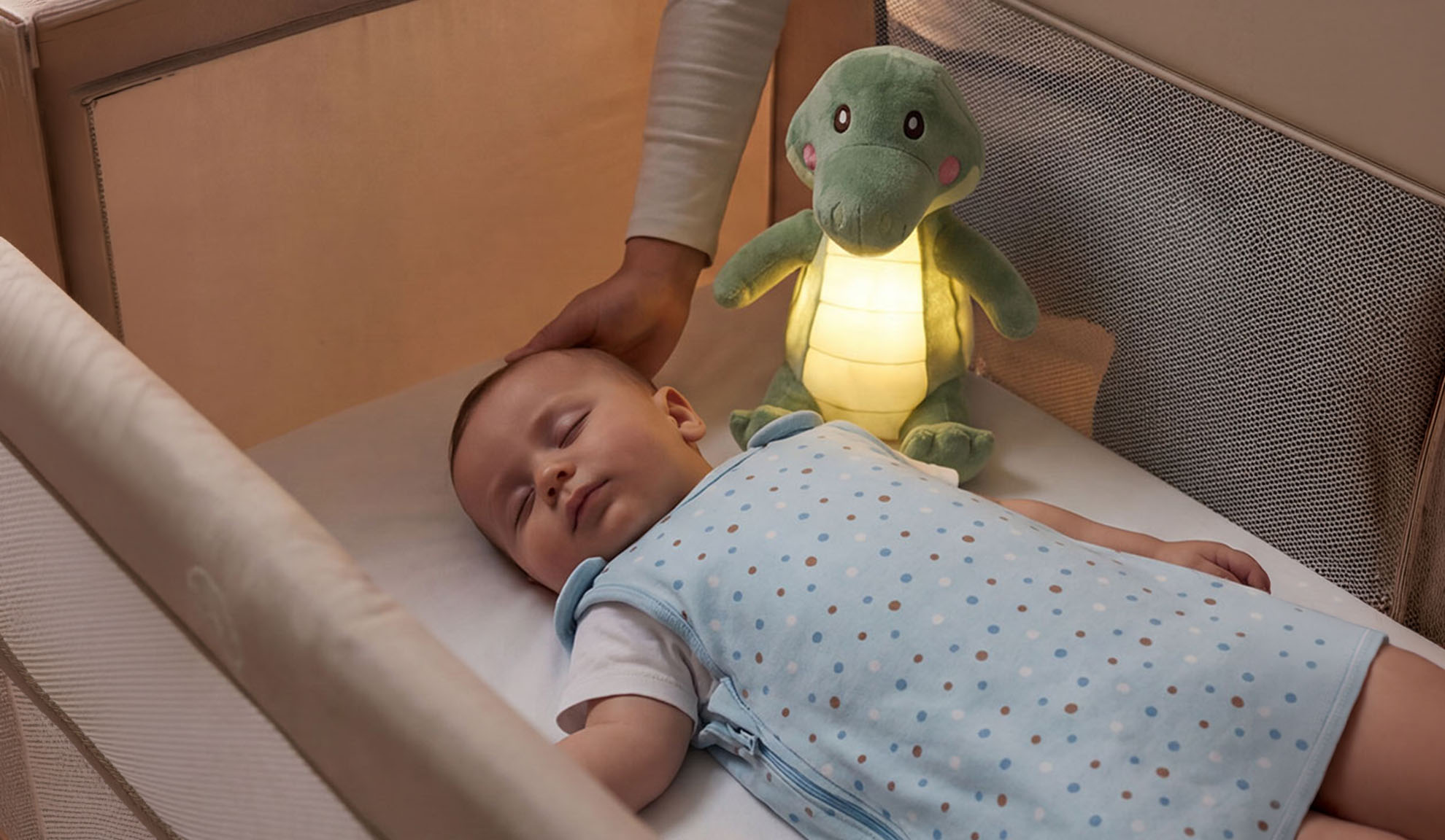 Bambino che dorme in culla con un peluche e la mano di un genitore.