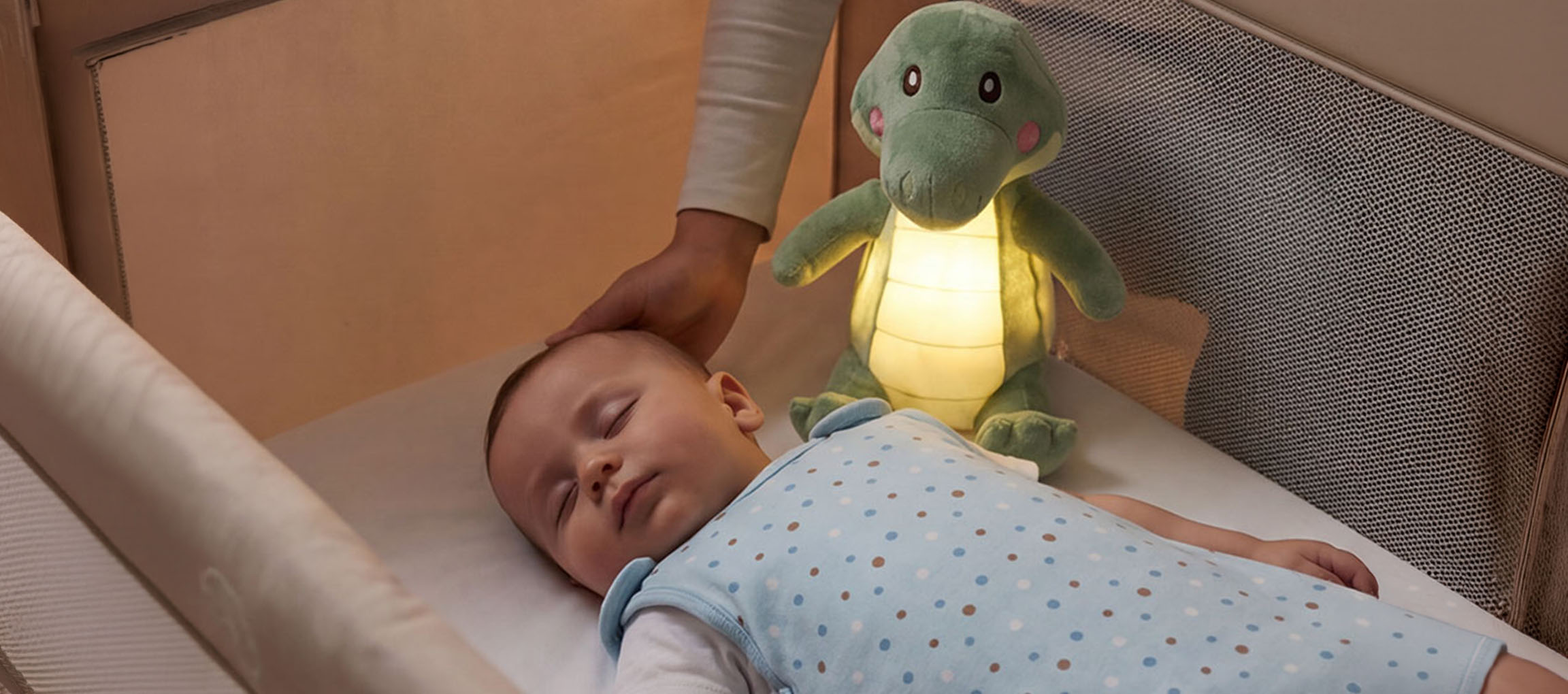 Bambino che dorme in una culla con una luce notturna di peluche, adulto che accarezza la testa del bambino.