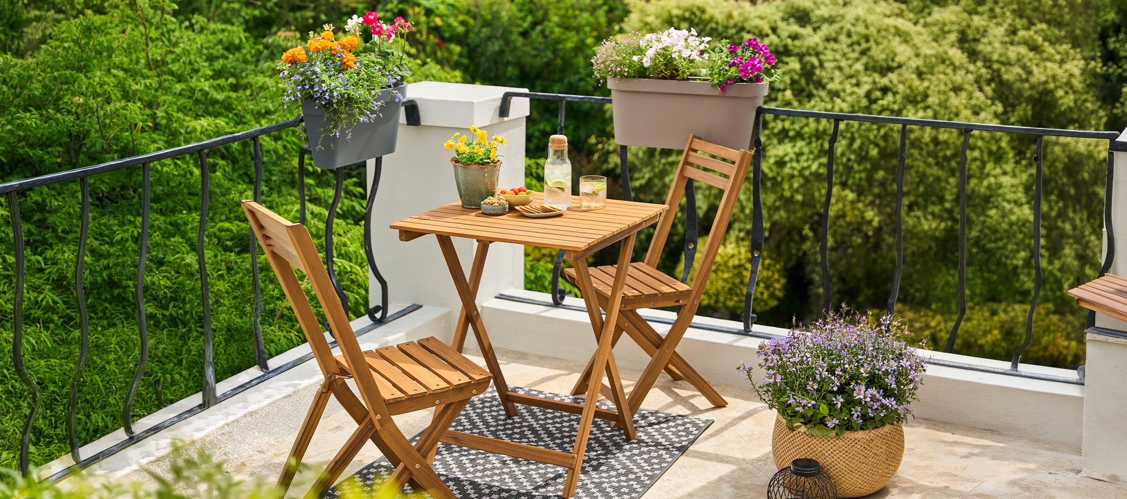 Set di mobili da balcone con tavolo e sedie pieghevoli, decorato con vasi di fiori.
