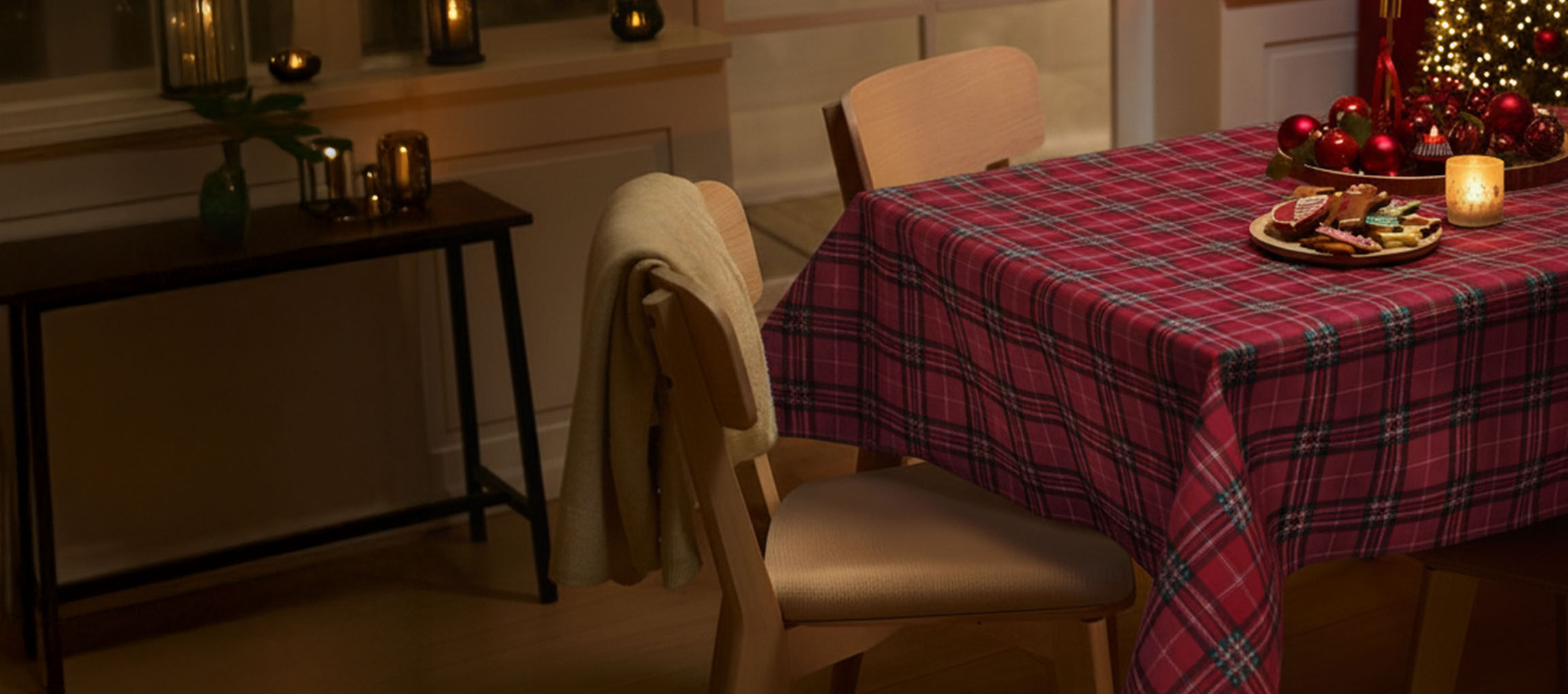 Tavola di Natale con tovaglia scozzese rossa, sedie e biscotti natalizi.