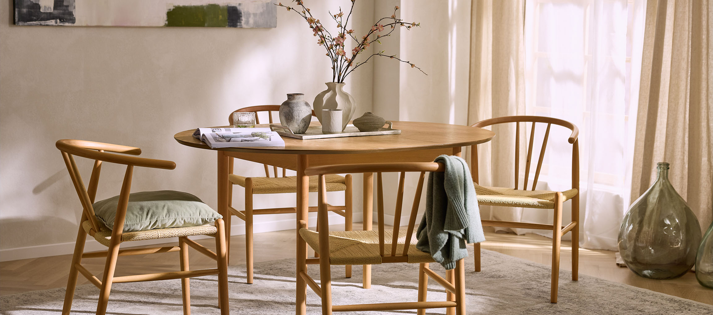 Sala da pranzo con tavolo rotondo in legno, sedie in legno con sedili in corda e vasi decorativi.