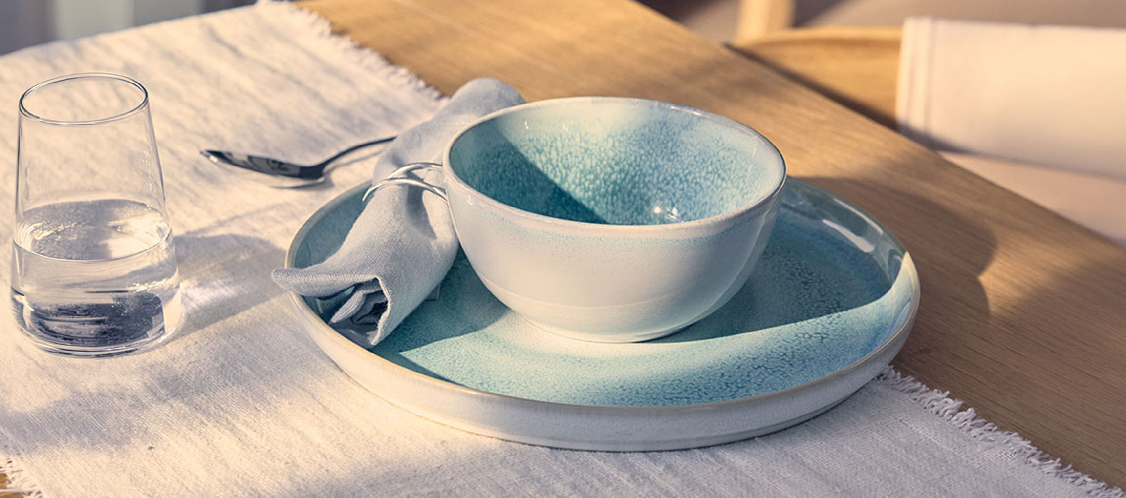 Tavola apparecchiata con ciotola e piatto in ceramica blu, bicchiere d'acqua e tovagliolo.