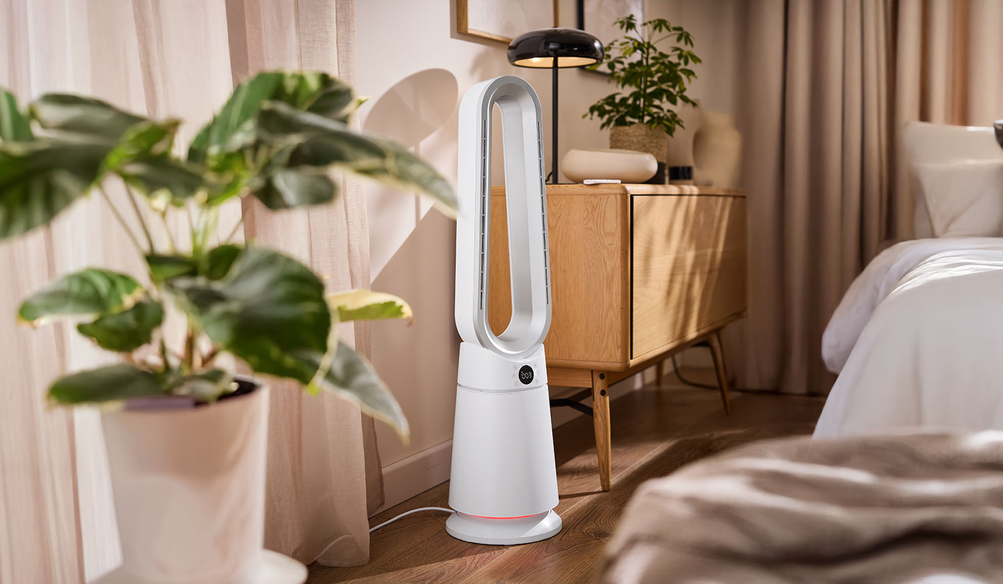 Ventilatore a torre bianco in una camera da letto moderna con piante e mobili in legno.