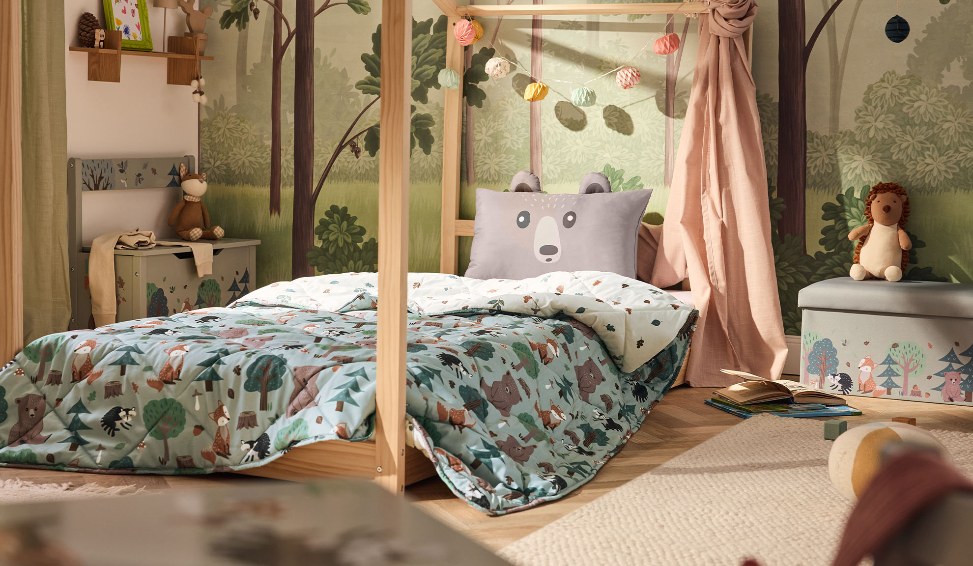Cameretta per bambini con letto in legno, cuscino a forma di orso e piumone a tema bosco.