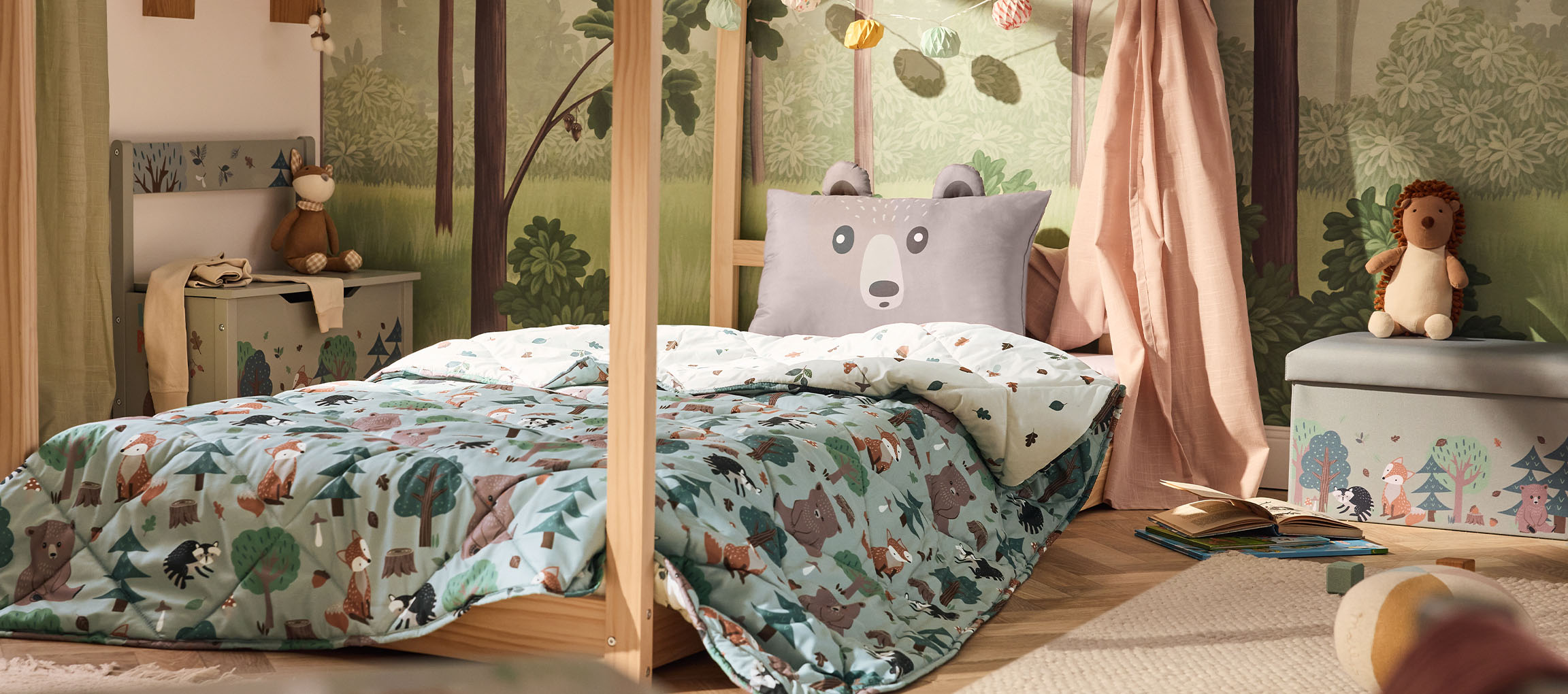 Cameretta per bambini con letto in legno, cuscino a forma di orso e piumone a tema bosco.