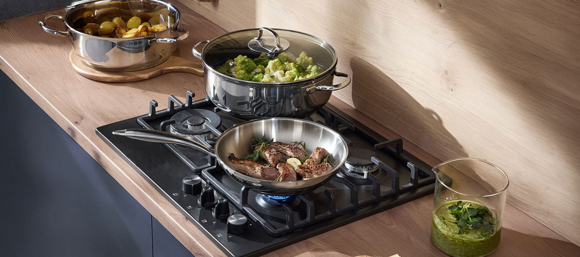 Piano cottura a gas con pentole e padelle in acciaio inossidabile piene di verdure e carne.