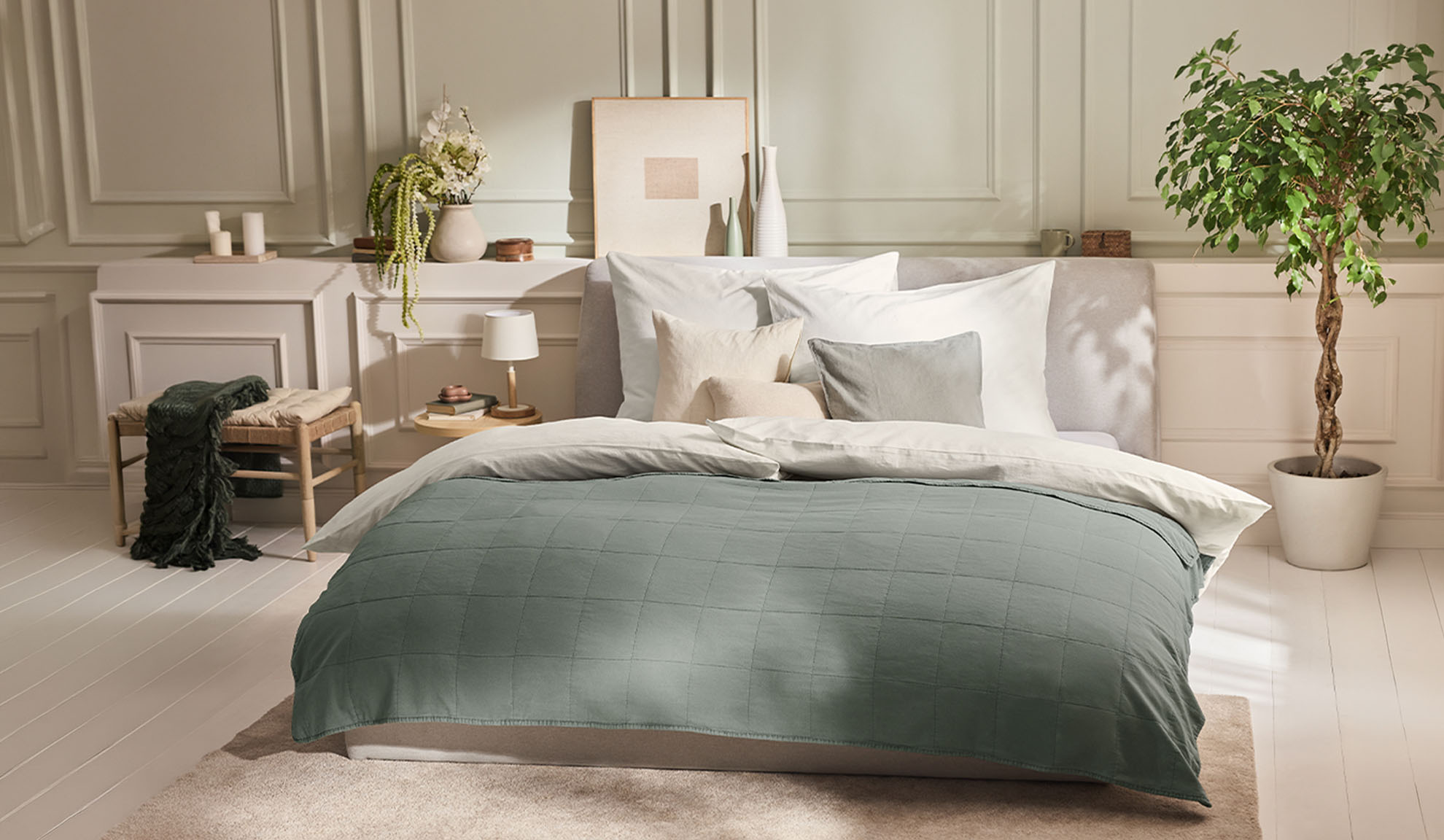 Camera da letto con letto, copripiumino verde, cuscini bianchi e una pianta