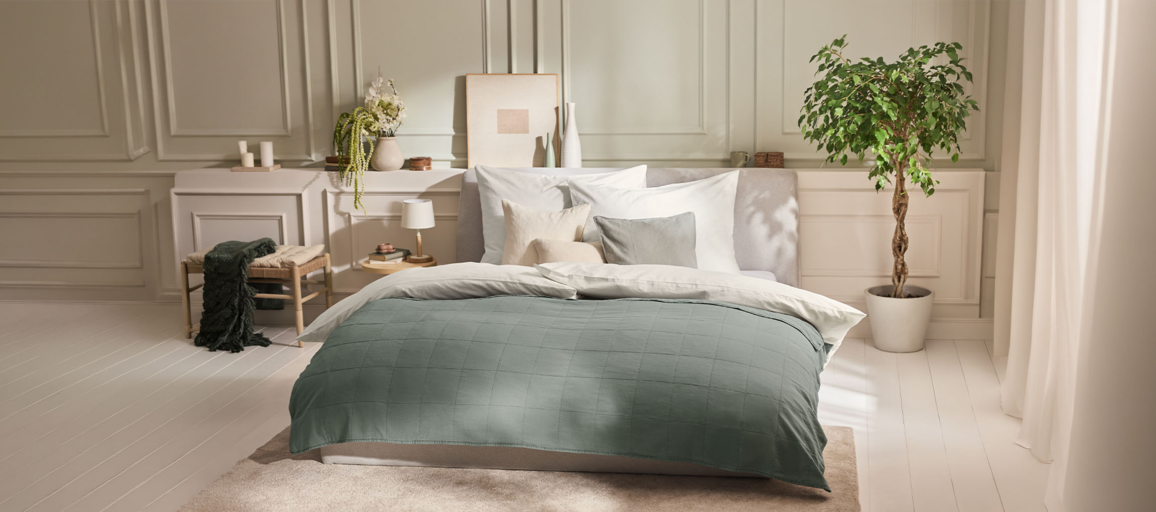 Camera da letto con letto, piumone verde, cuscini, comodino e una pianta.
