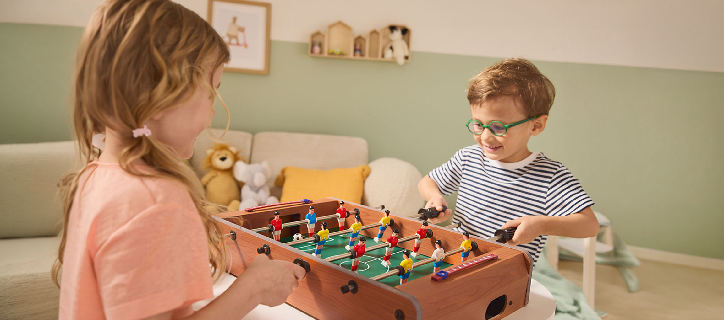 Due bambini giocano a calcio balilla, una bambina con una maglietta rosa e un bambino con una maglietta a righe.